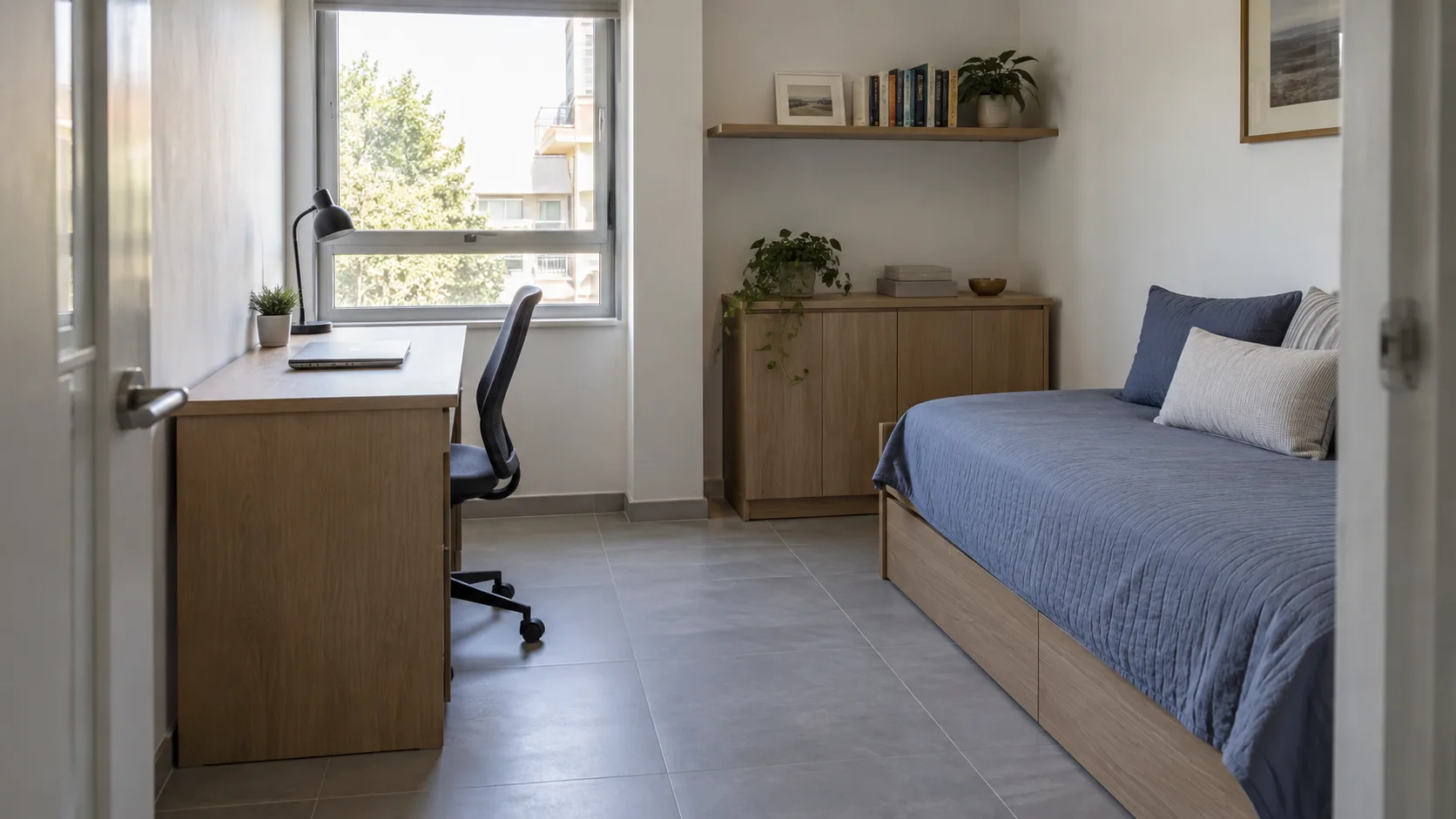 Small room with a desk beside the window, blue daybed and closed storage cabinet